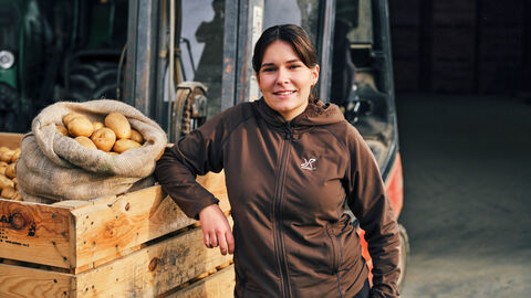 Das Bild zeigt Helena Wolf wie sie vor einem Traktor steht. Neben ihr sieht man eine Kiste voller Kartoffeln.